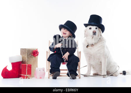 Golden Retriever (Canis lupus f. familiaris), petite fille habillé comme un ramoneur assis dans un fauteuil de toile entre noël décoration, une tirelire et un chien portant un top hat Banque D'Images