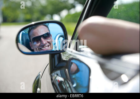 Le port de lunettes de soleil homme assis au volant de son cabriolet, qui se reflète dans le rétroviseur extérieur, Allemagne Banque D'Images