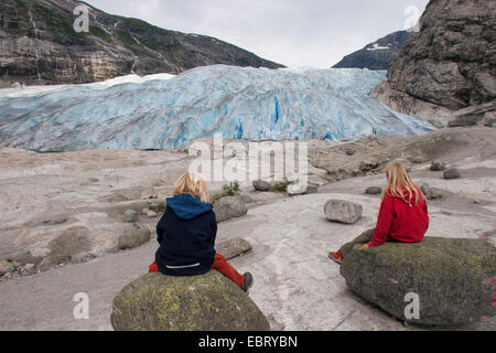 Deux enfants assis sur des rochers en face du glacier Nigardsbreen, la Norvège, le Parc National de Jostedalsbreen Banque D'Images