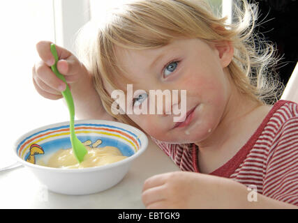 Petit garçon assis à la table et de manger de la crème anglaise, Allemagne Banque D'Images