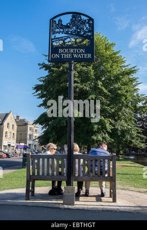 Les touristes en appui sur siège conducteur en panneau du village Bourton-on-the-Water Cotswolds Gloucestershire Banque D'Images