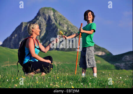 Garçon remise d'un bouquet de fleurs cueillies à sa mère durant la marche-tour dans les Alpes, France Banque D'Images