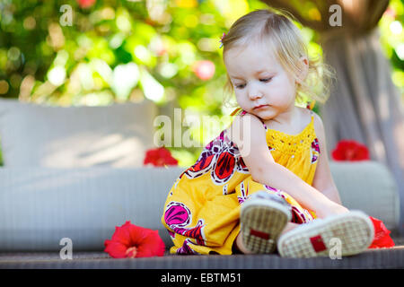 Petite fille portant un tissu d'été assis dehors sur un lit de camp Banque D'Images