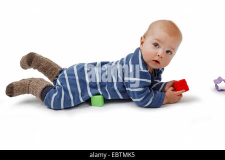 Petit garçon couché sur le ventre et de jouer avec les jouets de bébé Banque D'Images