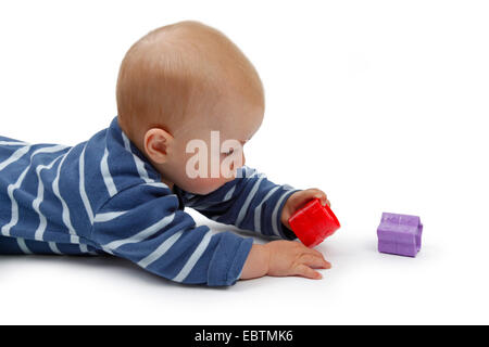 Petit garçon couché sur le ventre et de jouer avec les jouets de bébé Banque D'Images