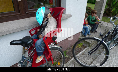 Trois petits garçons au retour d'un tour en vélo : deux d'alcool, l'un dormant dans le siège pour enfant sur un vélo Banque D'Images