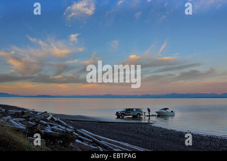 L'homme tirant son bateau de l'eau au coucher du soleil sur le détroit de Géorgie au nord de l'île de Vancouver, Comox, Côte Est du Canada Banque D'Images