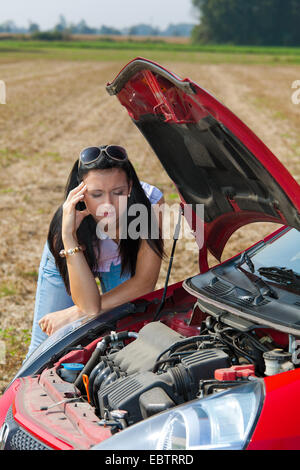 Jeune femme avec une panne de voiture cluelessly debout devant le moteur ouvert Banque D'Images