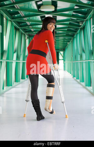 Jeune femme avec une jambe dans le plâtre et des béquilles est marcher dans un couloir Banque D'Images