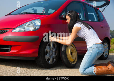 Jeune femme ayant une défaillance d'un pneu avec sa voiture est en train de changer un pneu Banque D'Images