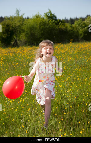 Happy little girl avec ballon de l'air à travers un pré, Allemagne Banque D'Images