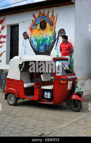 Chauffeur de taxi appuyé contre un mur de la maison en face de ses trois-roues en attente de clients, Guatemala, lac Atitlan, Santa Cruz la Laguna Banque D'Images