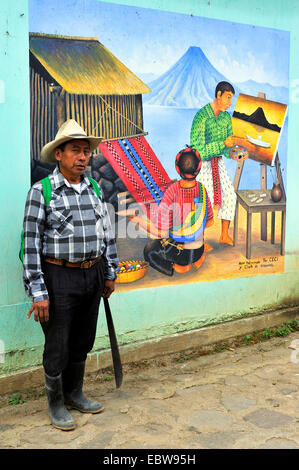 Homme avec une machette à la main est debout devant un tableau sur un mur de la maison montrant un homme d'avoir une vue et une femme tissant un tapis, Guatemala, lac Atitlan, Santa Cruz la Laguna Banque D'Images