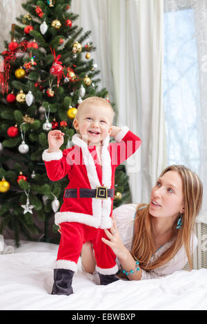 Jeune mère jouer avec bébé habillés en costume de Père Noël Banque D'Images