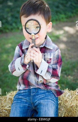 Cute Young Mixed Race Boy à la loupe par l'extérieur sur le foin en balles. Banque D'Images