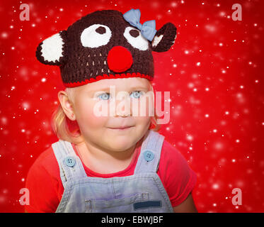 Closeup portrait of a little baby girl wearing hat Rudolph drôle sur fond de neige rouge, concept célébration de Noël Banque D'Images