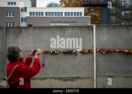 Femme de prendre une photo de fleurs placé dans le mur de Berlin au cours de 25e commémoration de sa chute Banque D'Images