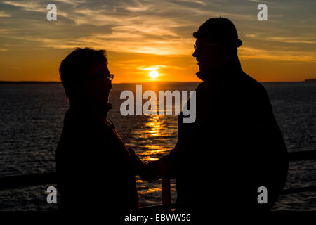Couple à la rambarde d'un navire devant le coucher de soleil sur la côte atlantique nord de Thurso, Ecosse, Royaume-Uni Banque D'Images