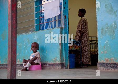 Petit garçon assis sur un pot en face d'un orphelinat, femme à l'intérieur, faire les lits, au Burundi, Bujumbura, Bujumbura Marie Banque D'Images