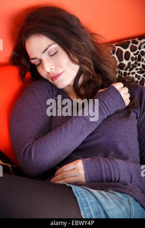 Brunette jeune femme assise sur un canapé sleeping Banque D'Images