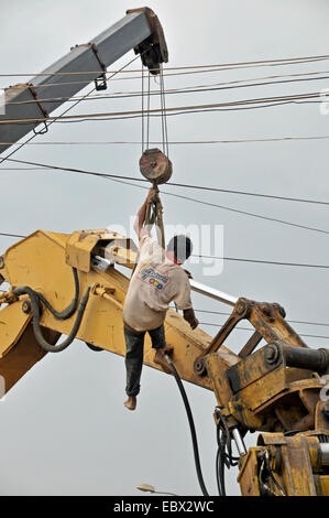 L'homme suspendu à une grue à réparer le bras d'une pelle excavatrice, Cambodge, Siem Reap Banque D'Images