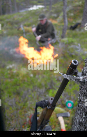 Le wapiti, l'orignal (Alces alces alces), hunter faire le café sur un feu de camp au cours d'une pause avec son fusil appuyé contre un arbre, la Norvège, Nord-Trondelag, Flatanger Banque D'Images