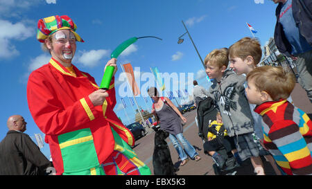 Clown de rue colorée vêtue de gonfler un ballon, les enfants le regarder, Pays-Bas, Noordwijk Banque D'Images