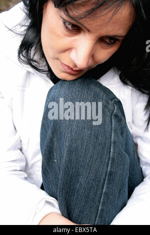 Yioung femme assise avec la tête s'appuya sur un genou perdu dans ses pensées Banque D'Images