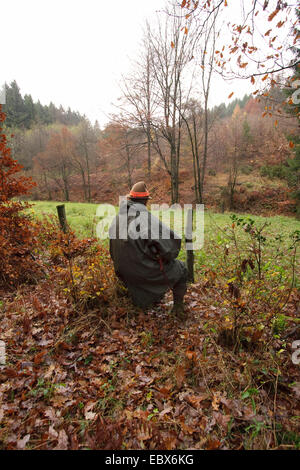 Hunter (shooter) assis et d'attendre avec le fusil en main lors d'une battue, Allemagne Banque D'Images