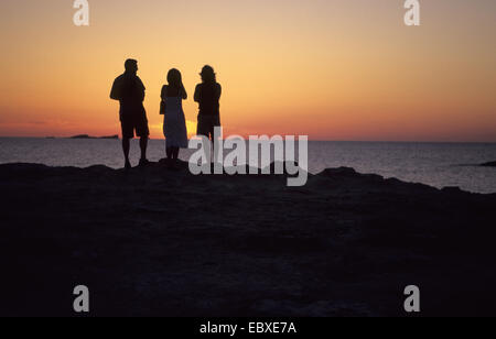 Trois personnes debout sur la rive à regarder le coucher du soleil, l'Espagne, Baléares, Ibiza Banque D'Images