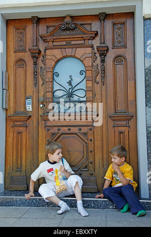 Deux garçons assis en face de la porte d'entrée et eating popcorn Banque D'Images