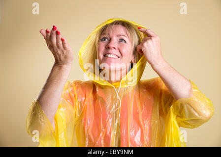 Femme portant un poncho jaune par temps humide tenant sa main pour vérifier s'il pleut Banque D'Images