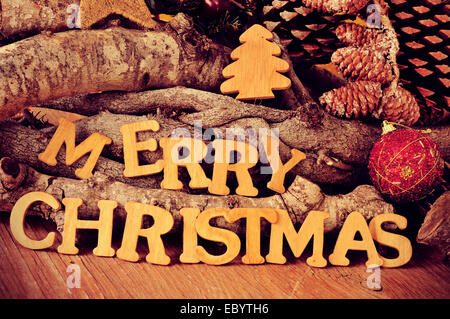 Lettres en bois formant la phrase joyeux noël sur une table en bois rustique avec des rondins et des pommes de pin dans l'arrière-plan Banque D'Images