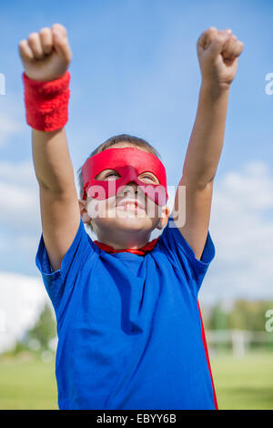 Garçon vêtu de cape et masque holding hands up et l'observation du soleil Banque D'Images