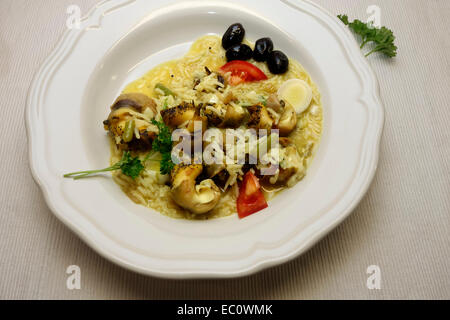 Risotto à la viande de bulots servis sur plaque blanche avec plus d'olives noires et de tomates. Banque D'Images