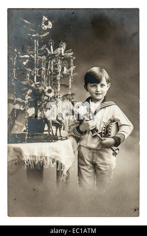 Happy boy avec arbre de Noël, cadeaux et jouets vintage photo sépia. Mobilier original avec du grain de film et des rayures Banque D'Images