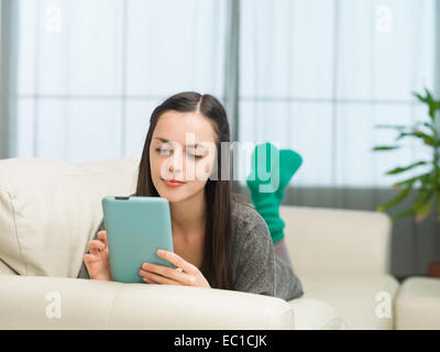 Beau young caucasian girl lying on sofa et jouer à des jeux sur tablette numérique Banque D'Images