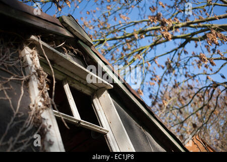 Détail de lucarne d'ossature de bois maison abandonnée avec le verre et manquant sur le réducteur séchées murs gris contre le ciel bleu Banque D'Images