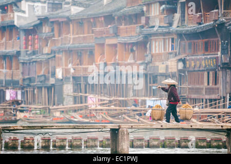 Hawker local traversant un pont en bois de l'autre côté de la rivière Tuojiang, Fenghuang, Chine Banque D'Images