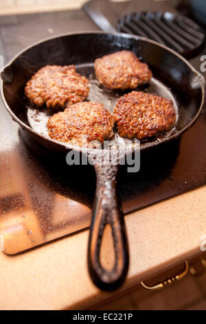 Petites galettes saucisse cuisson dans une poêle en fonte noire sur une cuisinière. Banque D'Images