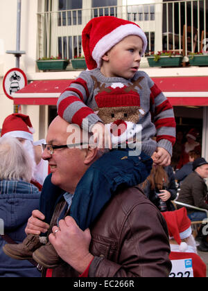 L'exécution de ton grand-père enfant portant un chapeau de Noël et de cavalier sur ses épaules, Padstow, Cornwall, UK Banque D'Images