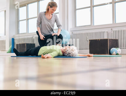 Femme thérapeute physique d'aider les femme avec exercice des jambes dans la thérapie de sport. Elder woman lying on floor étant assisté par Banque D'Images