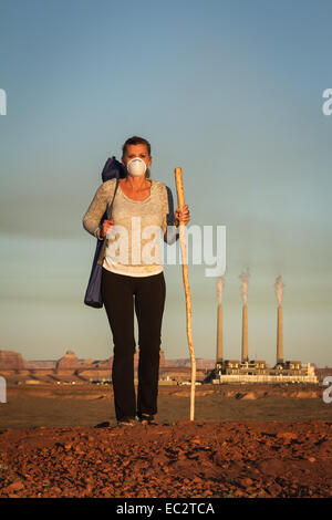 Notion de droit d'une femme portant un masque et un bâton de marche qui s'éloignent d'une centrale électrique au charbon avec fumée dans le Banque D'Images