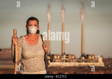Notion de droit d'une femme portant un masque et un bâton de marche qui s'éloignent d'une centrale électrique au charbon avec fumée dans le Banque D'Images