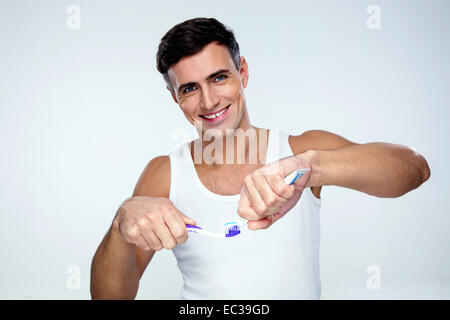 Happy man squeezing dentifrice sur une brosse à dents sur fond gris Banque D'Images