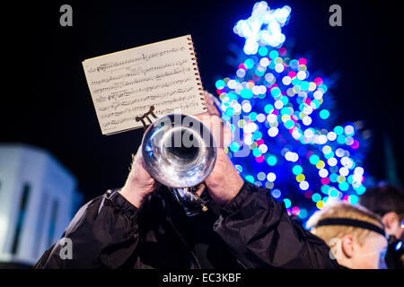 Un homme membre d'une fanfare jouant des chants de Noël sur un instrument trompette en laiton en face d'un grand arbre de Noël, UK Banque D'Images