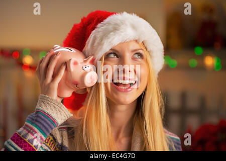 Portrait of smiling adolescent girl in santa hat avec piggy bank Banque D'Images