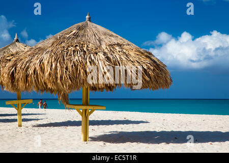 Couple en train de marcher au-delà de l'herbe parasols le long de la plage de sable blanc d'Eagle Beach, Aruba, Antilles Banque D'Images