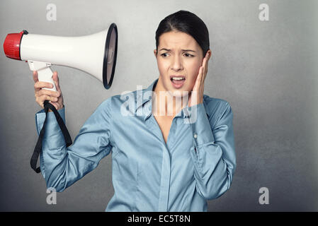 Jeune femme tenant un mégaphone à la tête et serrant son oreille d'une partie lésée à l'intensité de l'expression le son de façon à c Banque D'Images