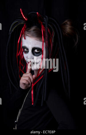 Fille avec doigt sur sa bouche passer pour devil in front of black background Banque D'Images